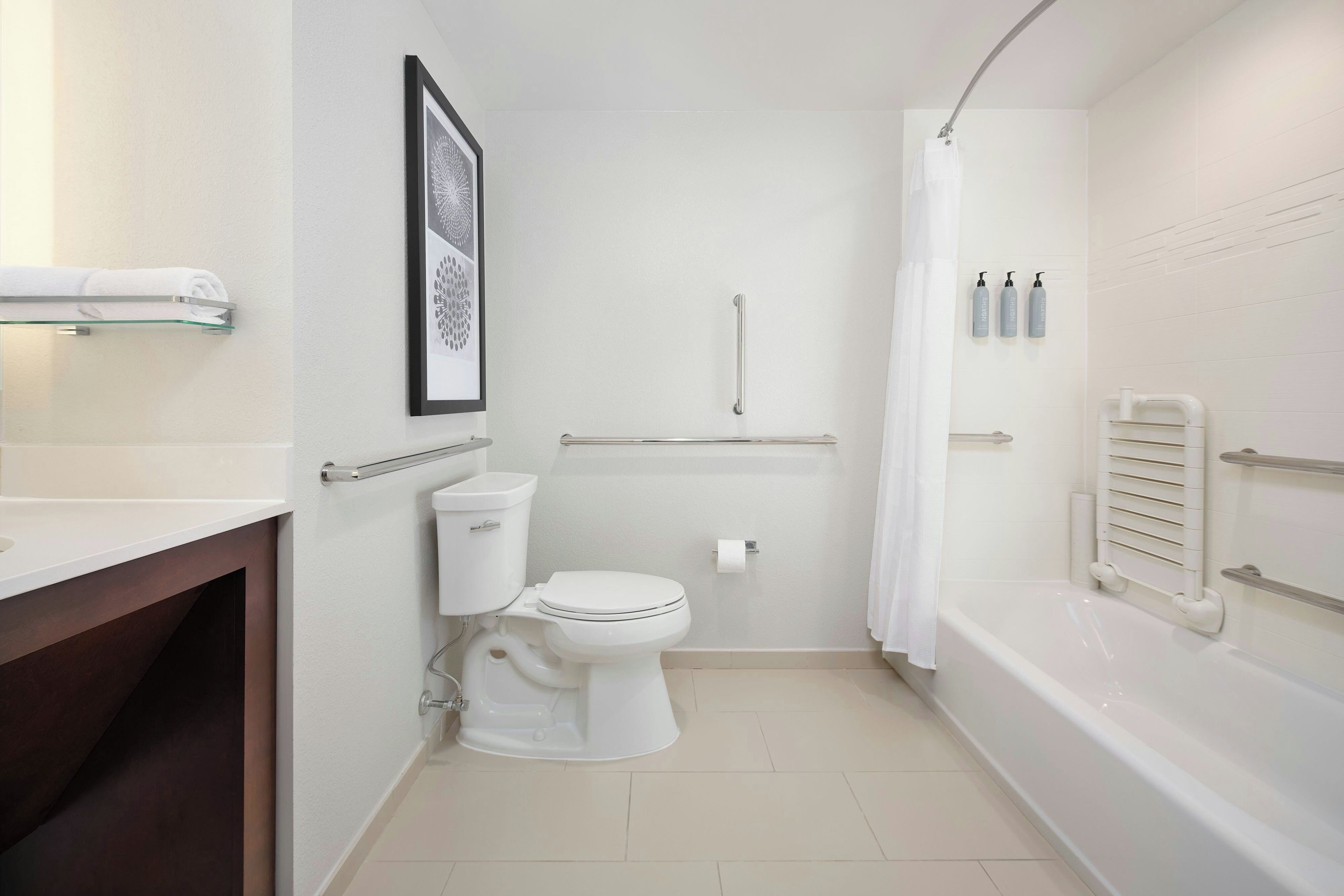 Une salle de bain comprenant des toilettes, une douche, une étagère en verre avec une serviette et un tableau encadré au mur.