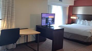 A hotel room with a bed, a desk, a chair, a television, and a window with curtains.