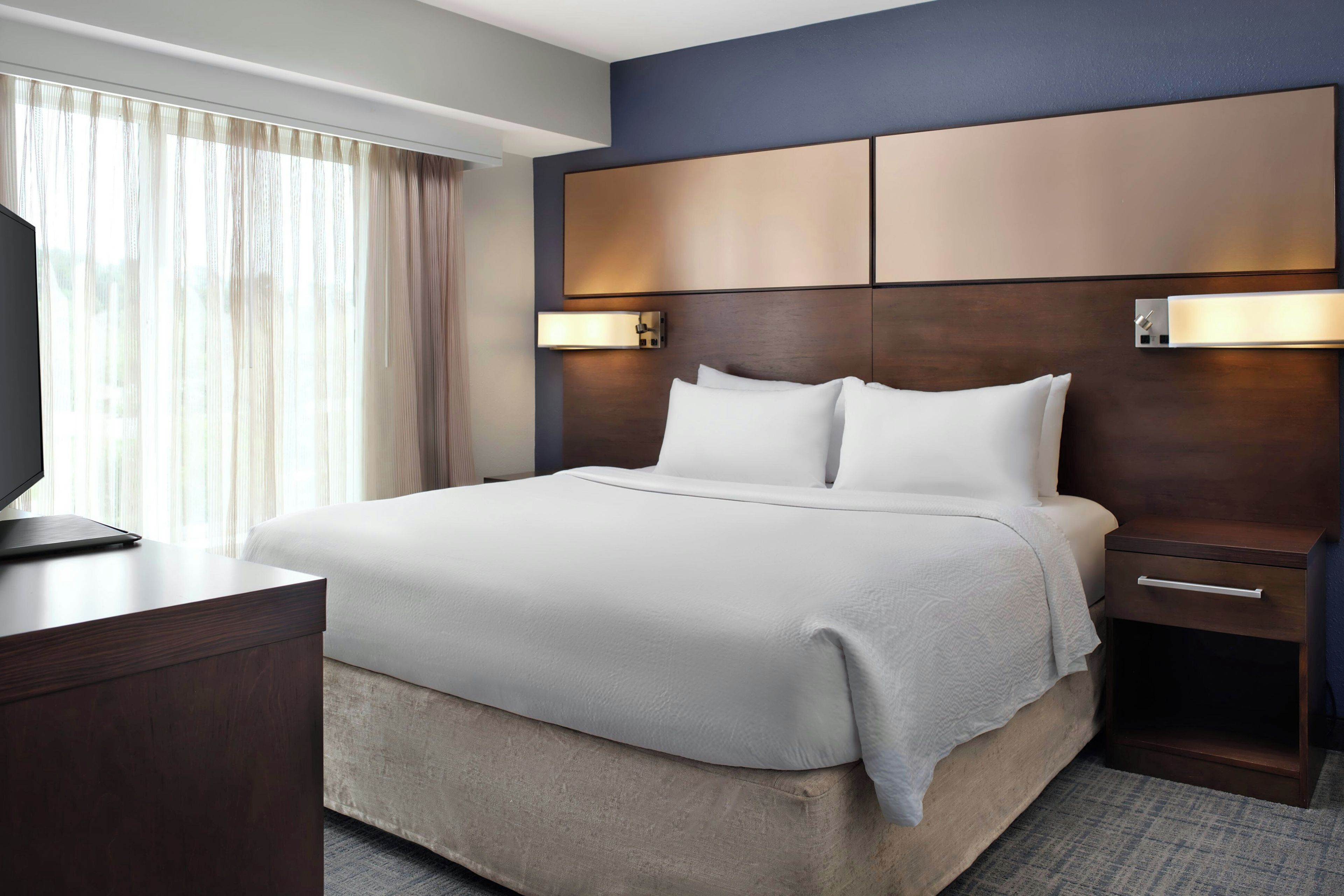 Una habitación de hotel con cama, mesitas de noche, escritorio y televisor.