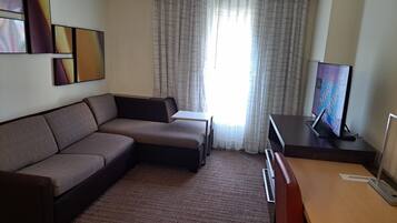 A modern living room with a sectional sofa, a flat-screen TV, and a large window with curtains.