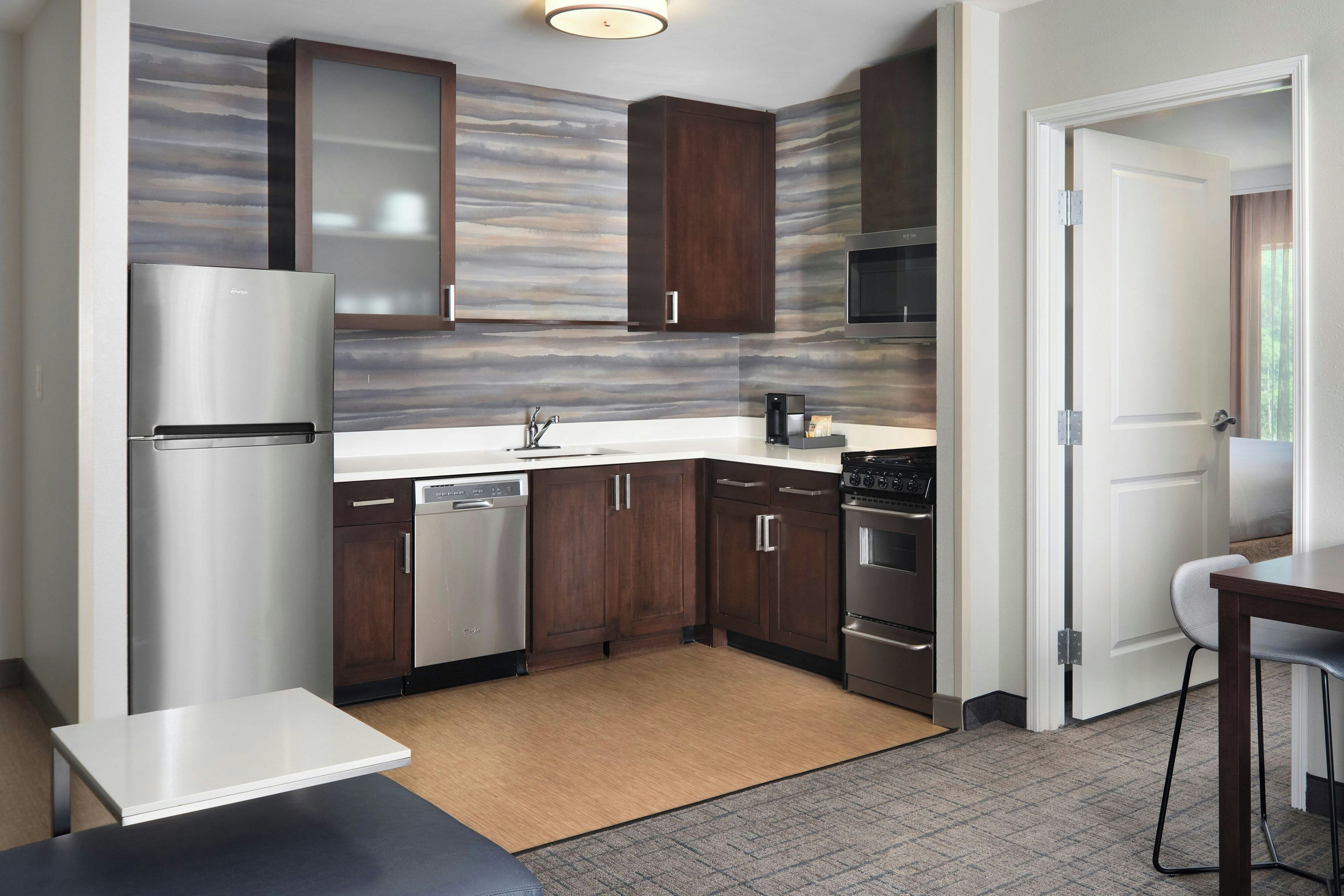 A modern kitchen with stainless steel appliances, dark wood cabinets, and a marble backsplash.