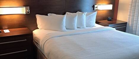 Quarto de hotel com uma cama grande, duas mesas de cabeceira, cabeceira com iluminação integrada e ar-condicionado fixado na parede.