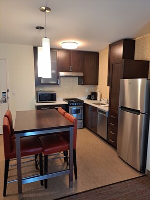 A modern kitchen with stainless steel appliances, a dining table with red chairs, and wooden cabinets. - Residence Inn Columbia West/Lexington (West Columbia)