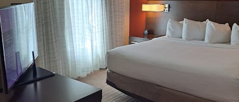 Une chambre d’hôtel comprenant un lit, un bureau avec un ordinateur, une table de chevet, une lampe et une fenêtre avec des rideaux.