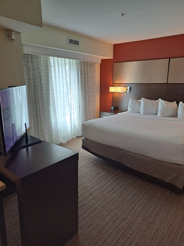 Une chambre d’hôtel comprenant un lit, un bureau avec un ordinateur, une table de chevet, une lampe et une fenêtre avec des rideaux.