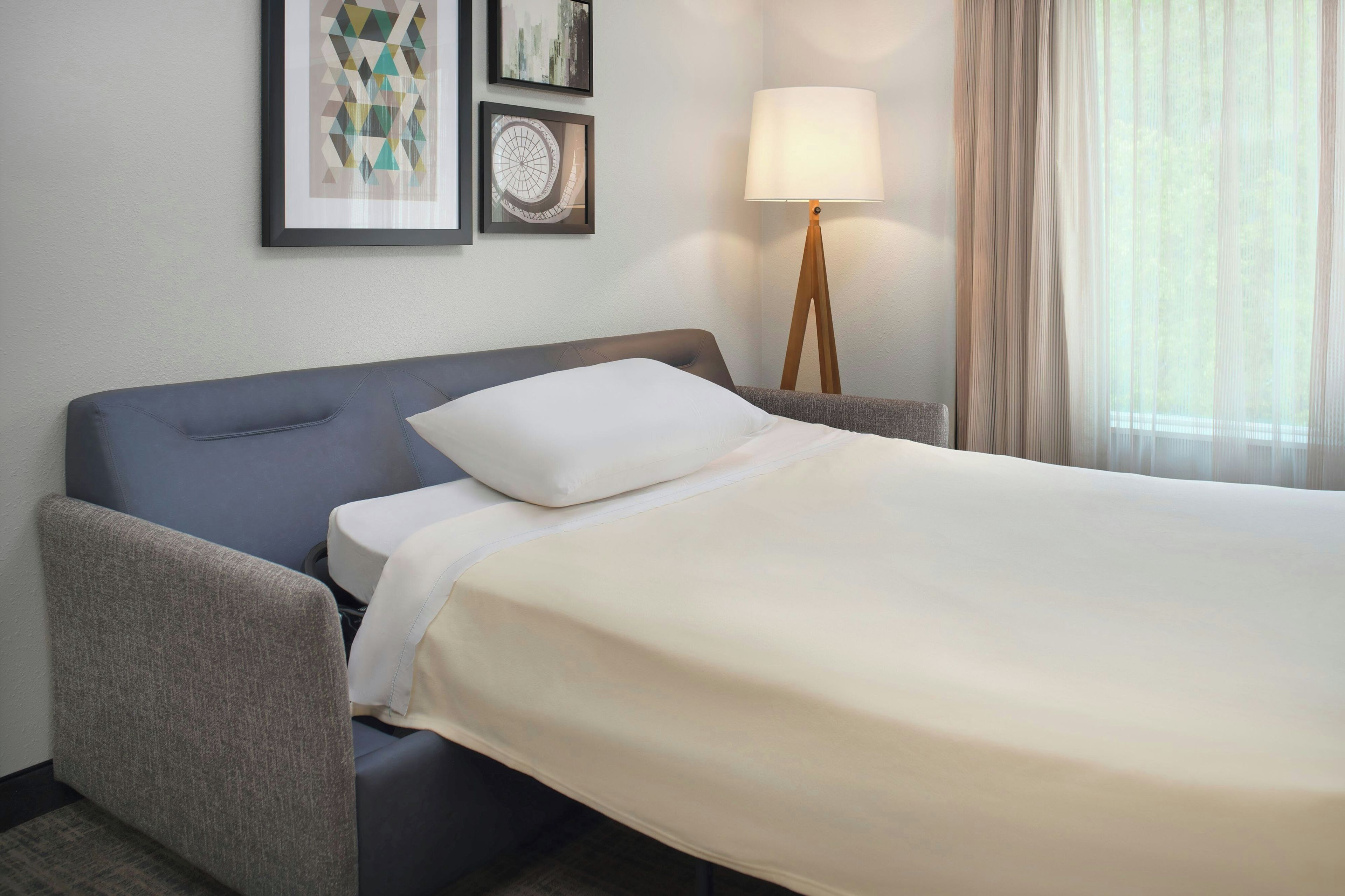 Une chambre d’hôtel avec un lit, une chaise, une lampe et des œuvres d’art accrochées au mur.
