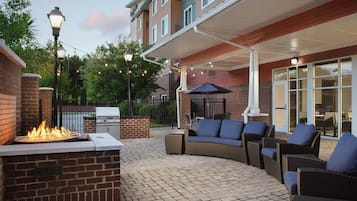 Une terrasse extérieure avec un barbecue en briques, des meubles en osier et des guirlandes lumineuses.