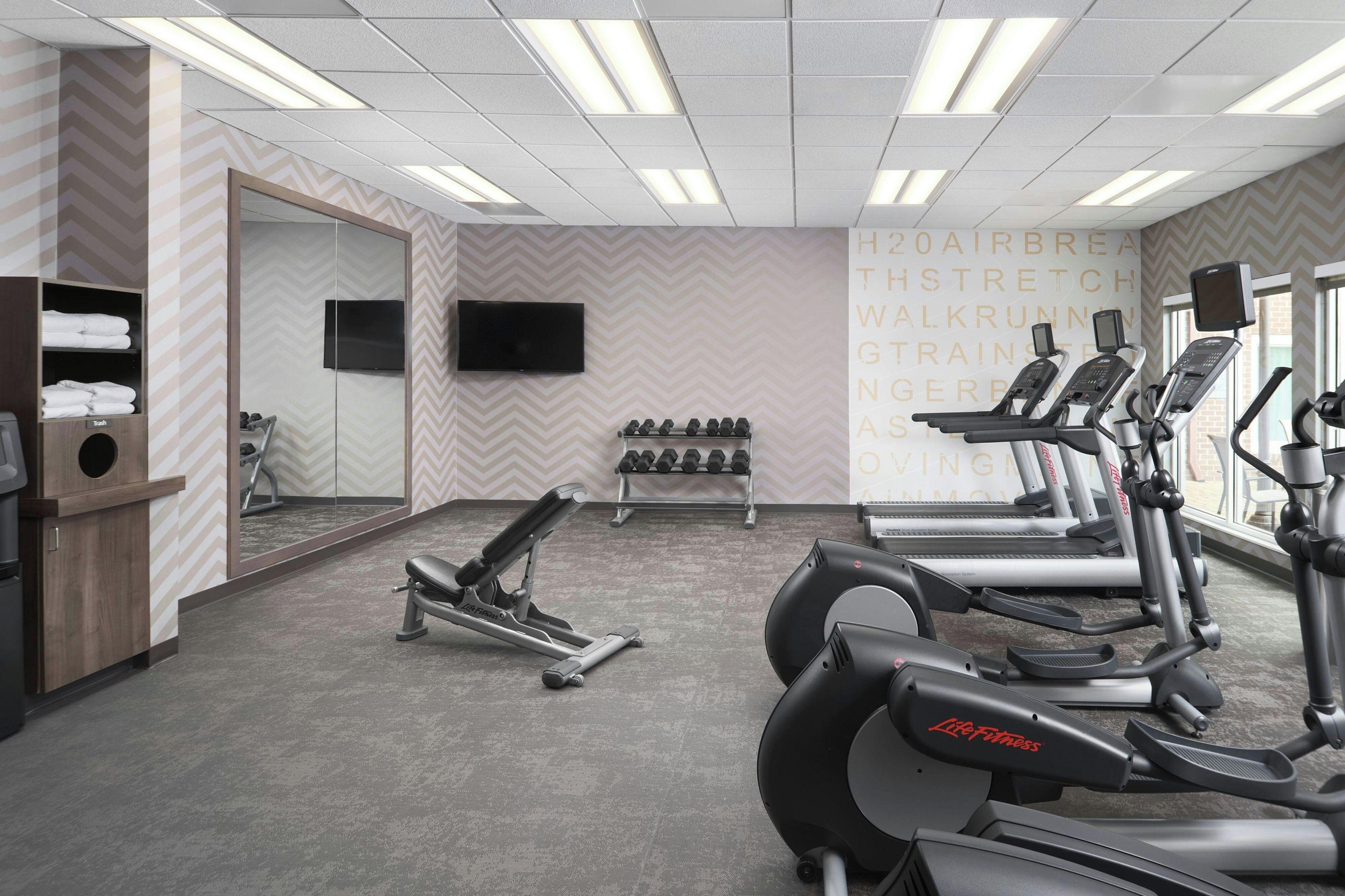 A gym with treadmills, dumbbells, and a TV on the wall.