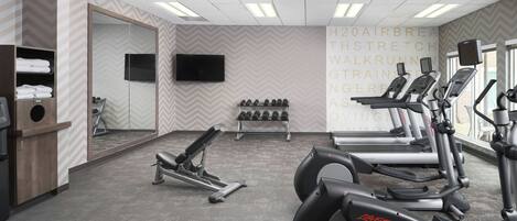 A gym with treadmills, dumbbells, and a TV on the wall.