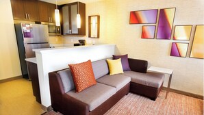 A modern living room with a brown sectional sofa, a white coffee table, and a kitchen area with stainless steel appliances. - Residence Inn Columbia West/Lexington (West Columbia)