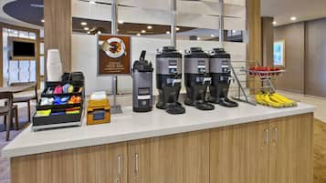 Una estación de café con varias cafeteras y una cesta de fruta.
