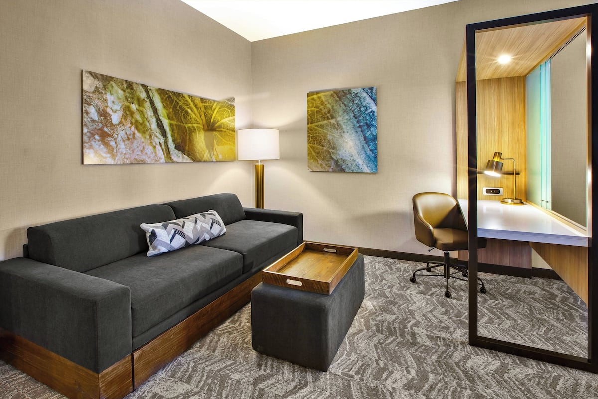 A modern hotel room with a sofa, ottoman, desk, chair, and artwork on the walls.