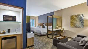 Een hotelkamer met een kitchenette, een bed, een slaapbank en een grote spiegel.