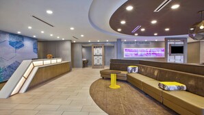 Een moderne lobby met een receptiebalie, een zithoek en een groot digitaal scherm.