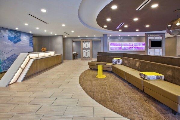 A modern lobby with a reception desk, seating area, and a large digital display.
