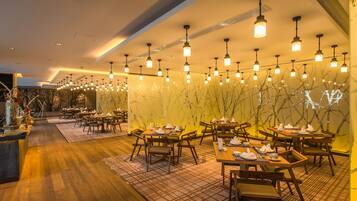 A restaurant with wooden tables and chairs, hanging pendant lights, and a marble wall with a tree design.