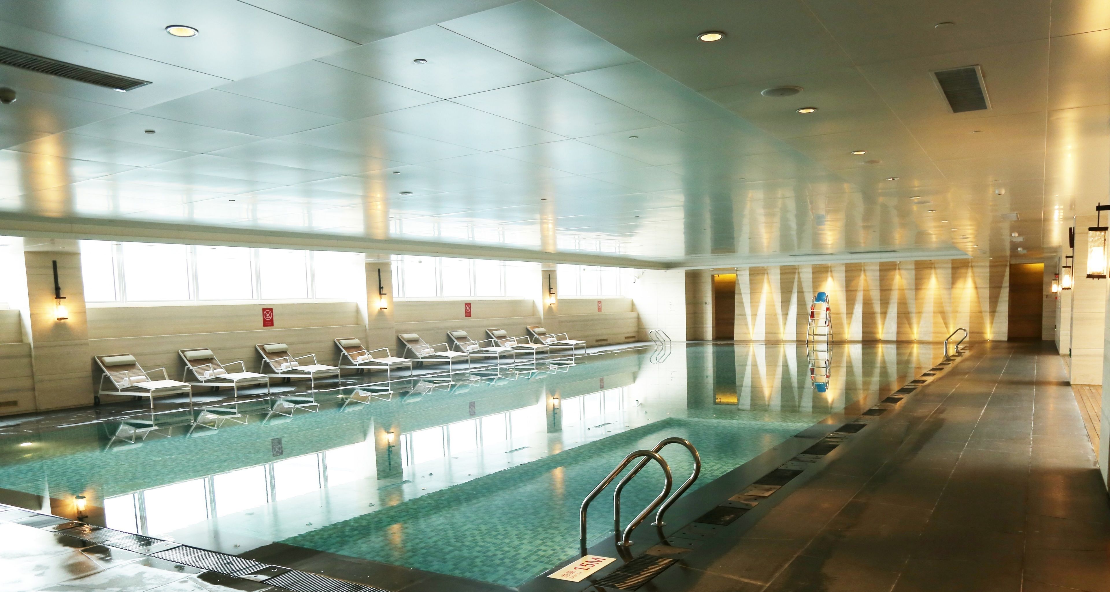 A large indoor swimming pool with multiple lanes, sunlit ceiling, and lounge chairs along the side.
