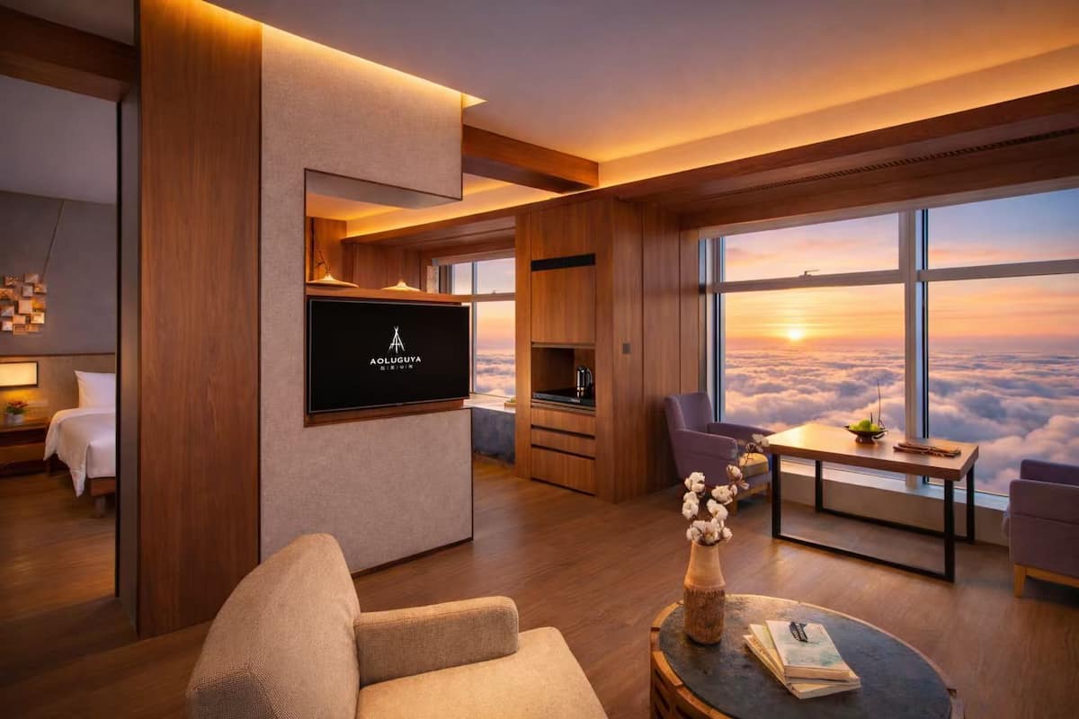 Ein modernes Hotelzimmer mit großem Fernseher, bequemen Sitzmöglichkeiten, einem Essbereich und Blick auf die Wolken.