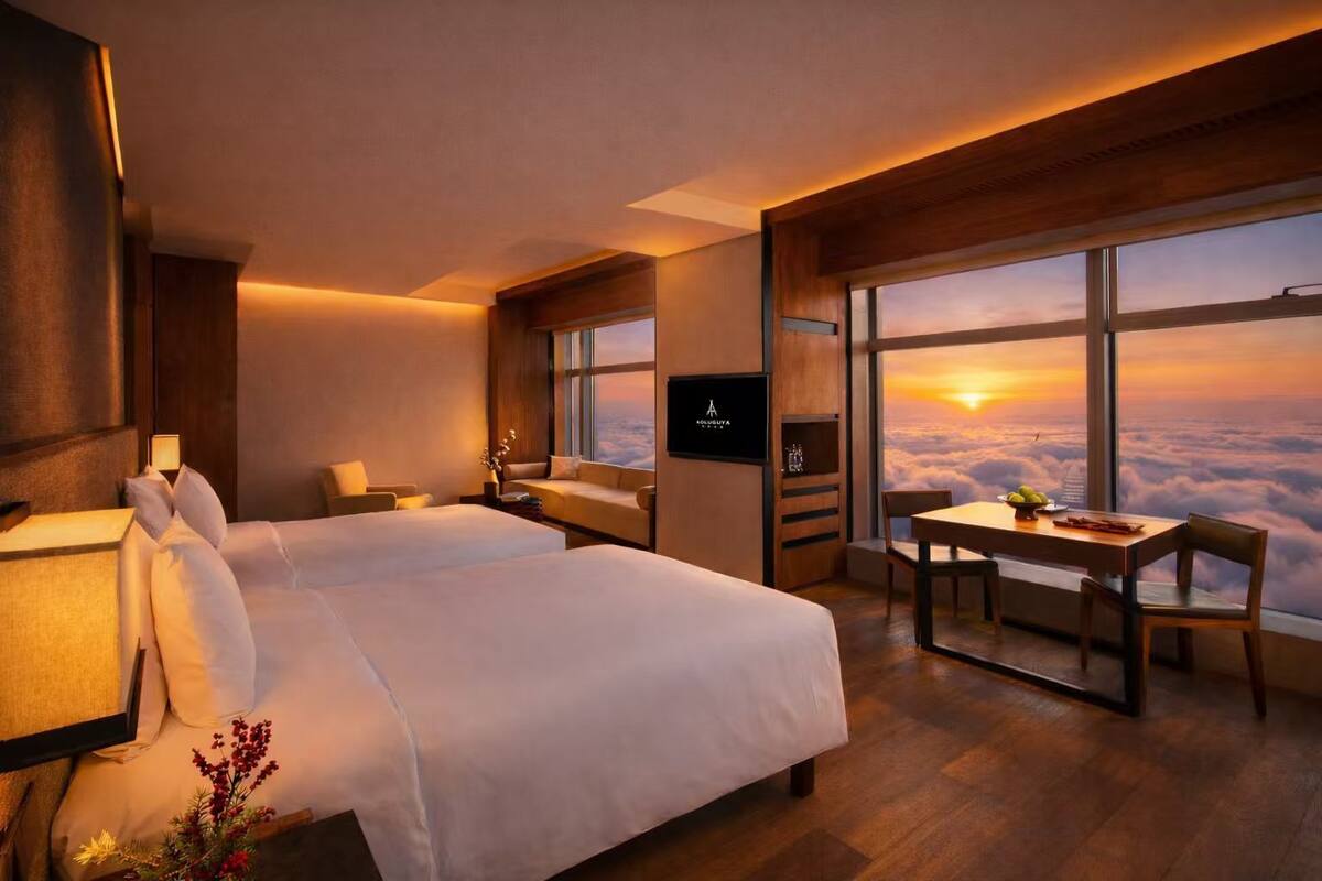 Ein Hotelzimmer mit einem großen Bett, einem Schreibtisch und Blick auf den Sonnenuntergang.