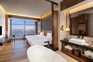 Habitación de hotel con una cama grande, un sofá independiente, una bañera, un tocador con espejo y vistas a la ciudad.