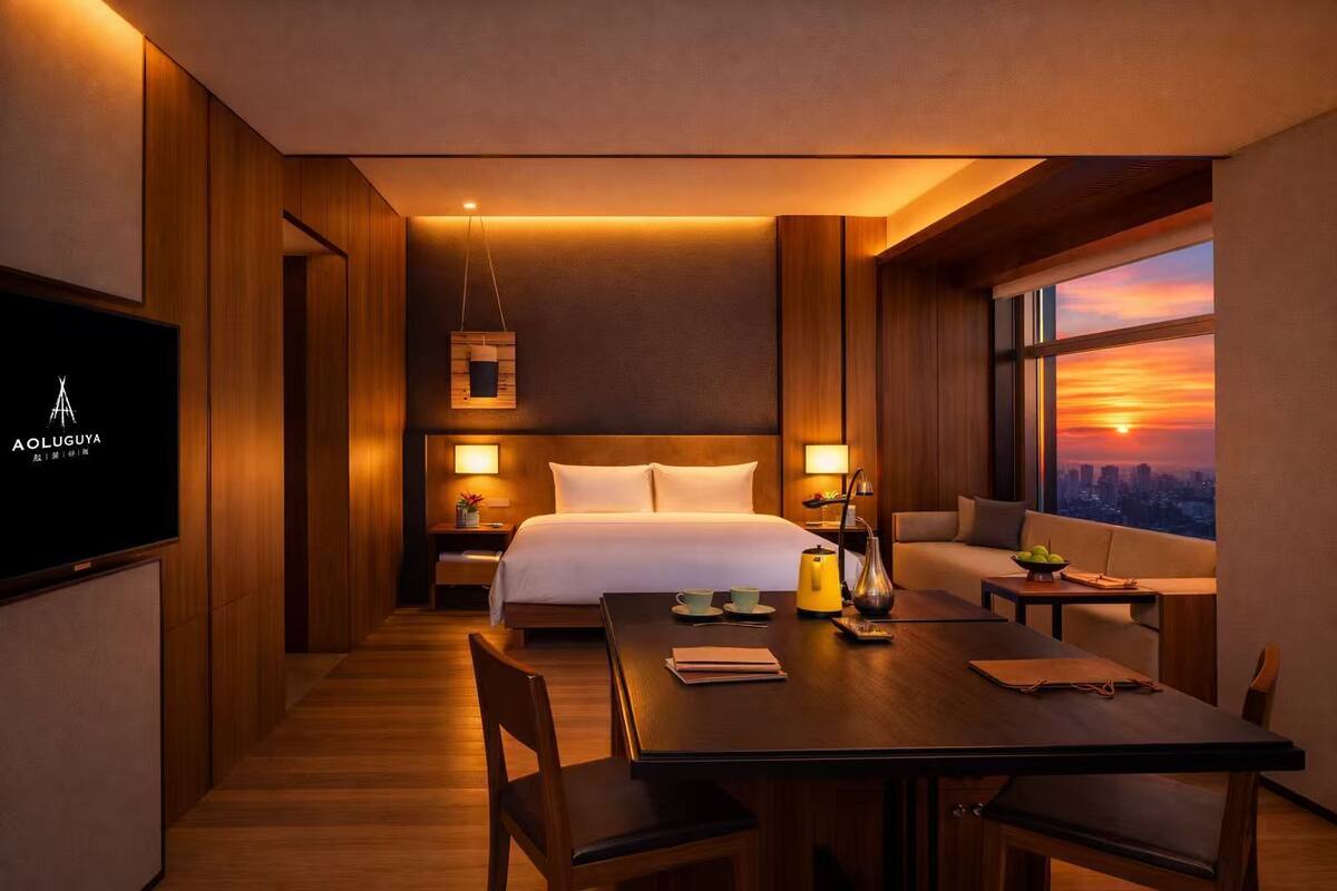 Ein Hotelzimmer mit Bett, Nachttischen, einem Schreibtisch mit Stühlen, einem Fernseher und Blick auf einen Sonnenuntergang über der Stadt.