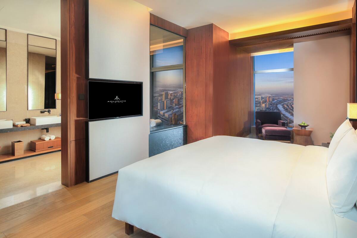 Ein Hotelzimmer mit Bett, Fernseher, Badezimmer und Blick auf die Stadt.