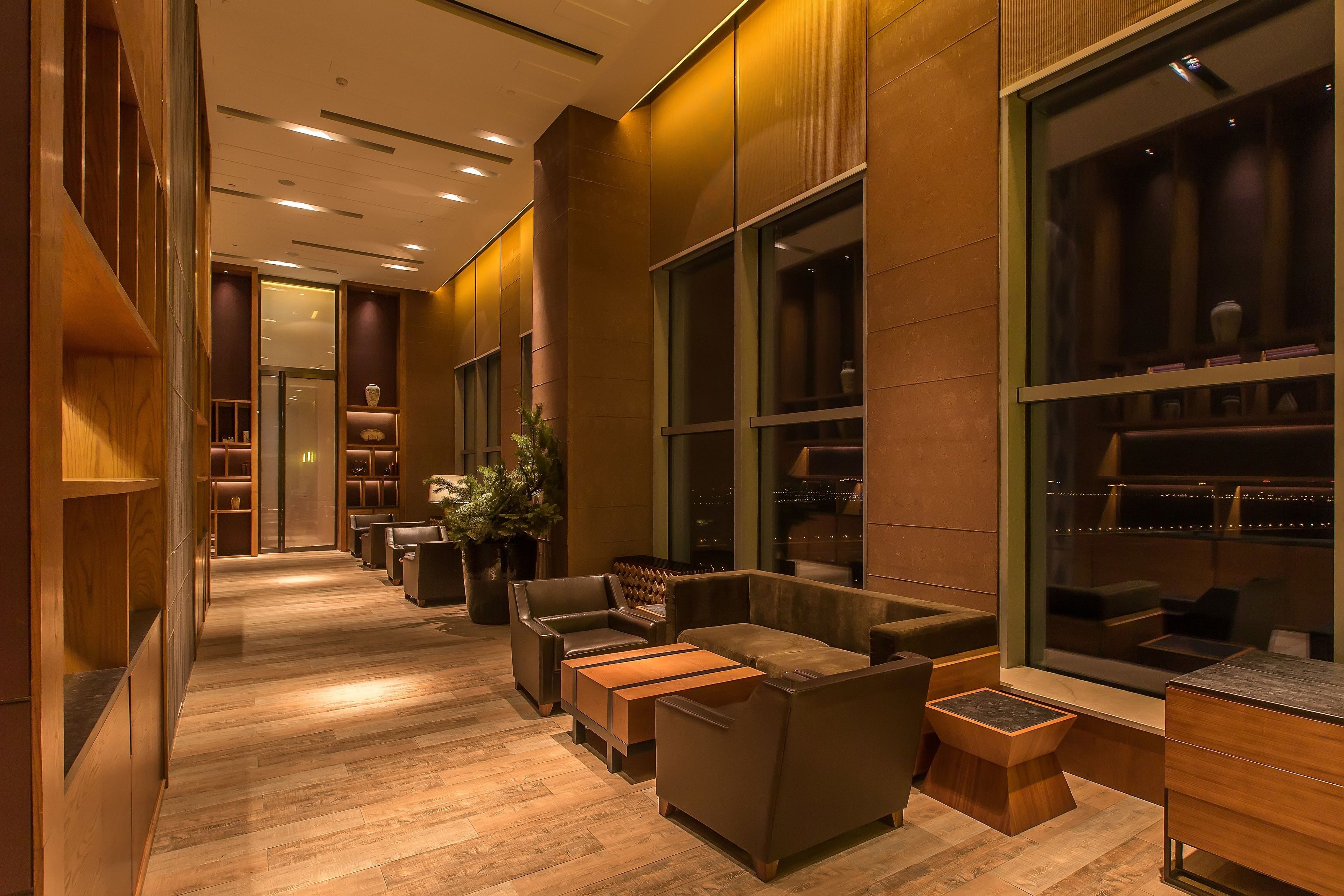 A modern hotel lobby with wooden flooring, seating areas, and large windows.