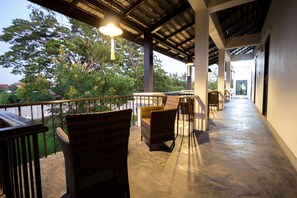 A covered outdoor area with wicker furniture and a view of trees. - Jamadevi Hotel (Lamphun)