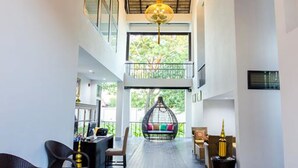 A spacious interior with a high ceiling, a central hanging light fixture, and a balcony with a view of greenery. - Jamadevi Hotel (Lamphun)