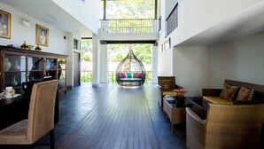 A spacious indoor area with a high ceiling, a balcony with a hanging chair, and a seating area with wicker furniture. - Jamadevi Hotel (Lamphun)