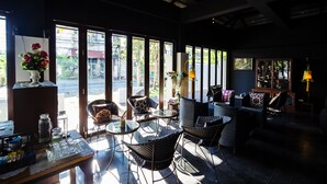 A well-lit indoor seating area with wicker furniture, large windows, and a view of the outside. - Jamadevi Hotel (Lamphun)