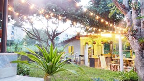 An outdoor seating area with string lights, wooden tables, and chairs, surrounded by greenery and trees. - Squirrel Hostel (Chiang Mai)
