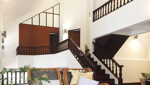 A spacious living area with a wooden staircase, wicker furniture, and potted plants. - Squirrel Hostel (Chiang Mai)