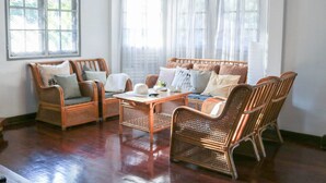 A room with a wooden floor, wicker furniture, and a large window with a view. - Squirrel Hostel (Chiang Mai)