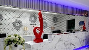 Un comptoir d’accueil surmonté d’un plateau en marbre, une sculpture abstraite rouge et un arrangement floral.