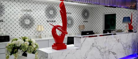 A reception desk with a marble top, a red abstract sculpture, and a floral arrangement.