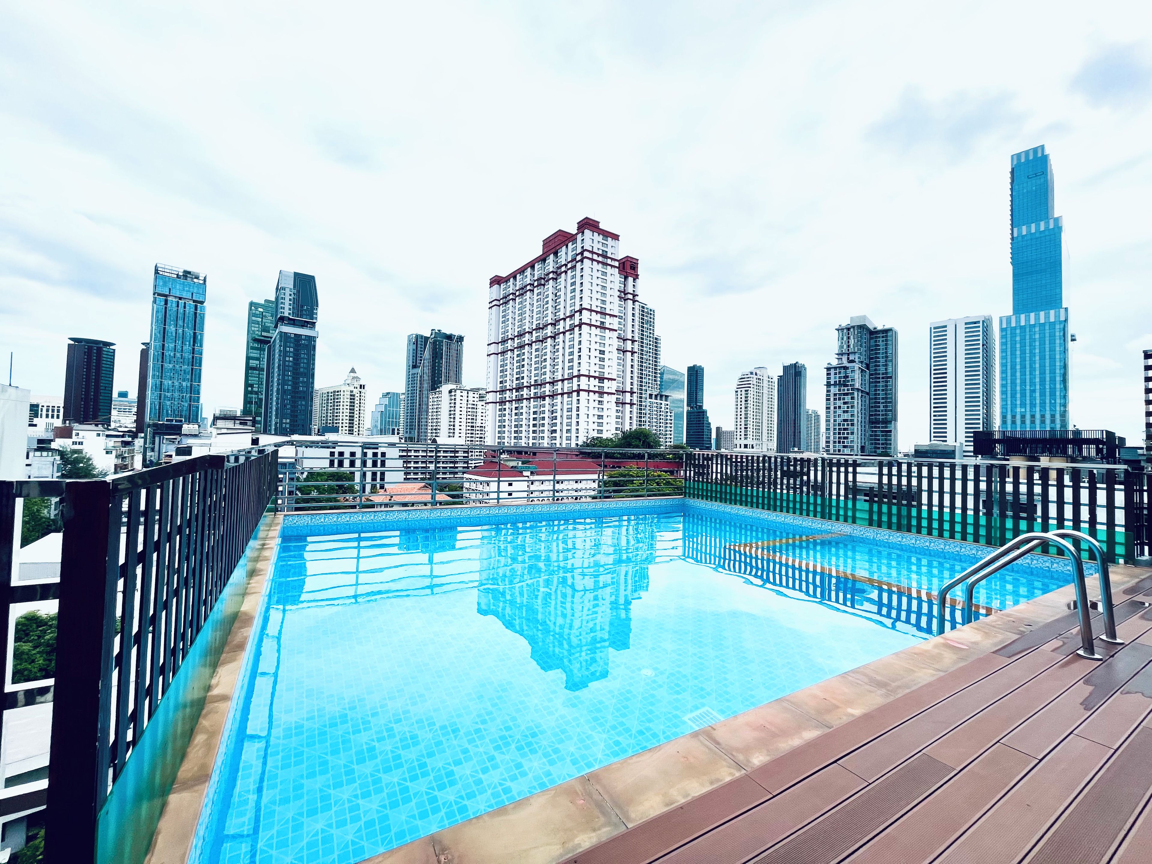 A rooftop pool with a city skyline view, surrounded by a wooden deck and metal railing.