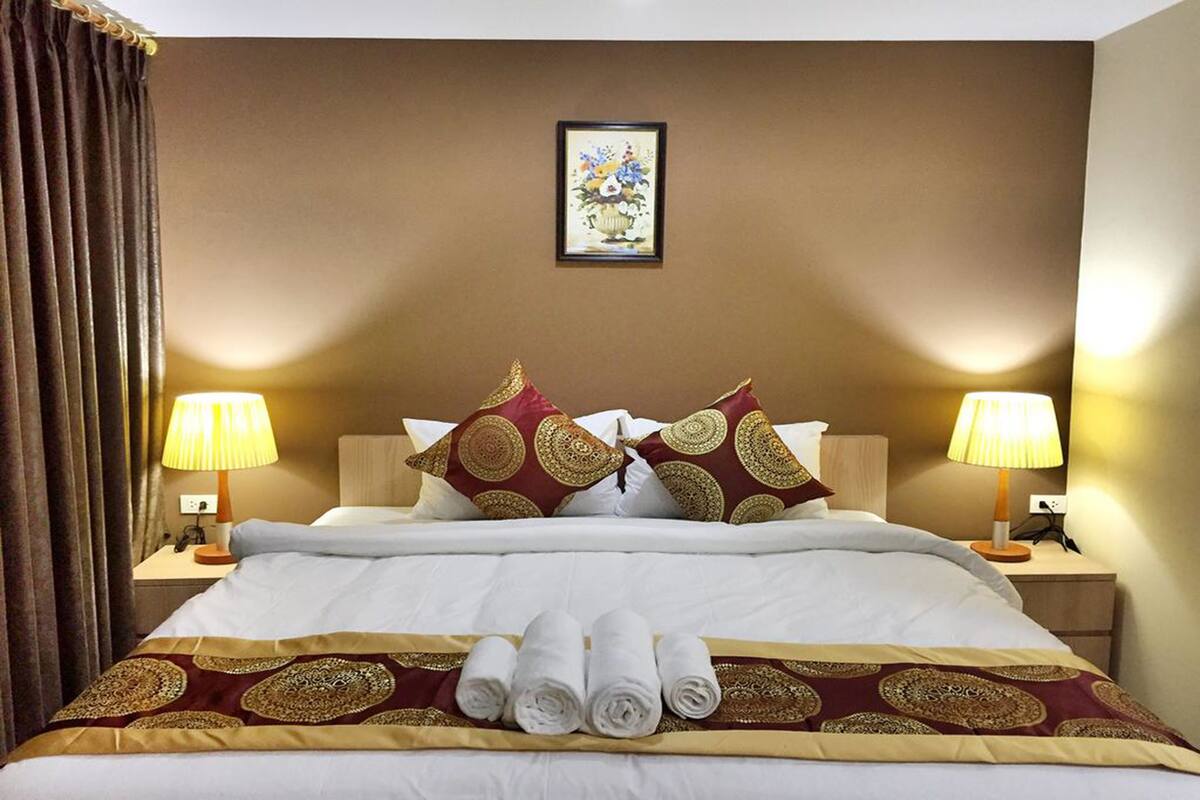 Hotelkamer met een groot bed, twee bedlampen, een lijst aan de muur en een stapje opgerolde handdoeken op het bed.