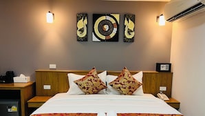 Une chambre d’hôtel avec un lit soigneusement fait, deux coussins décoratifs, un climatiseur fixé au mur et une œuvre d’art murale au-dessus du lit.