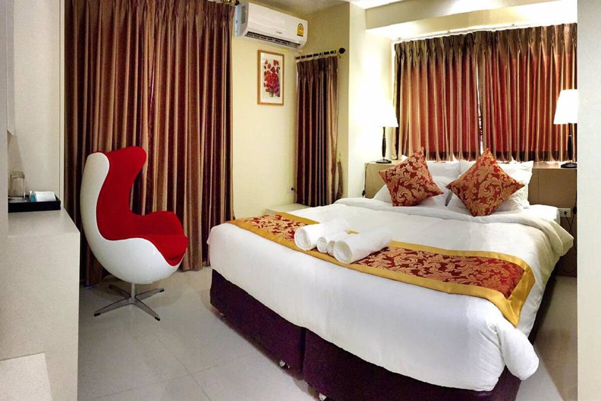 Een hotelkamer met een bed, een rode stoel en een groot raam met gordijnen.