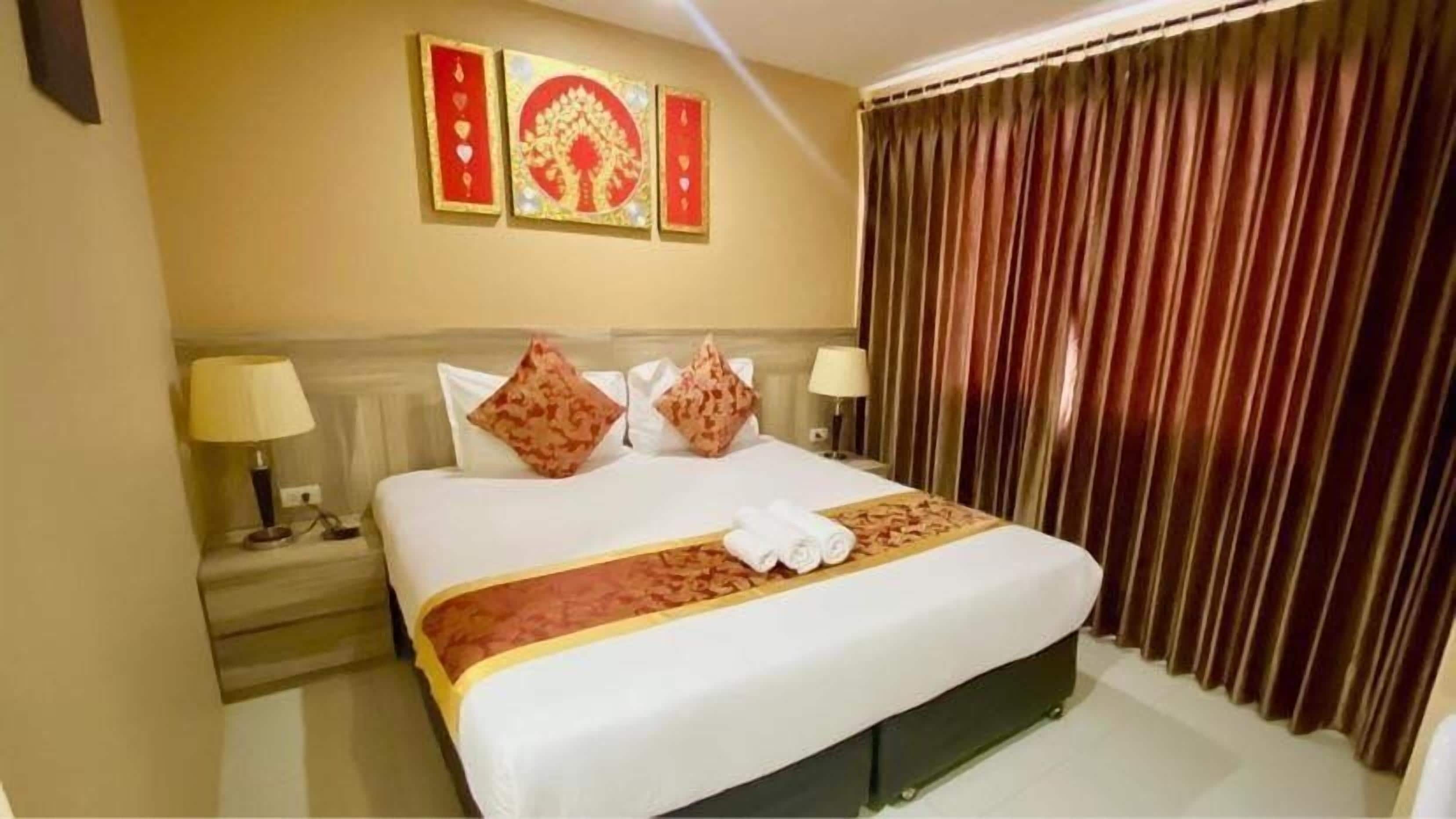 A hotel room with a large bed, two pillows, a bedside table with a lamp, and a curtain.