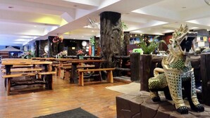 A spacious indoor area with wooden benches and tables, a decorative tree trunk, and a statue of a mythical creature. - A2Sea Hotel (Pattaya)