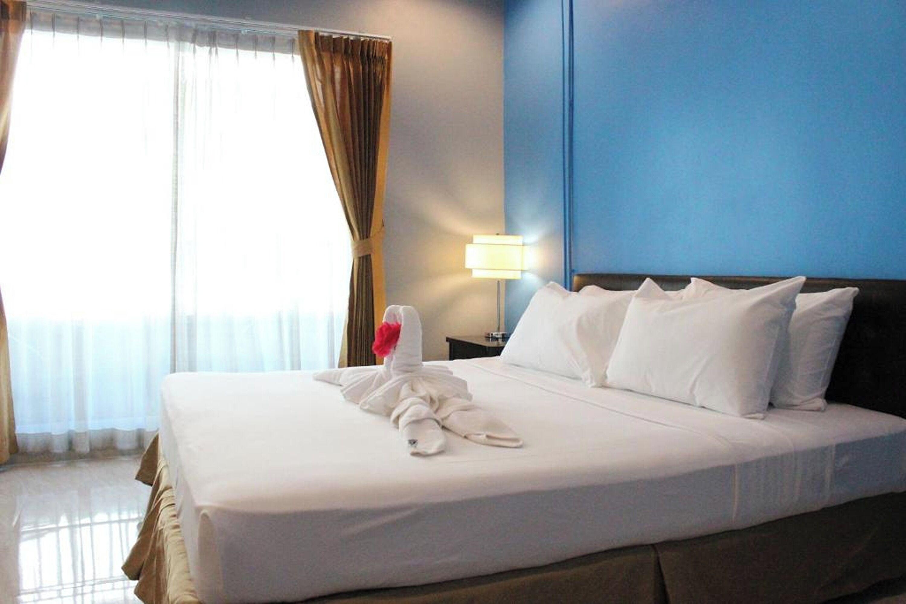 A hotel room with a neatly made bed, a lamp on the nightstand, and a window with curtains.