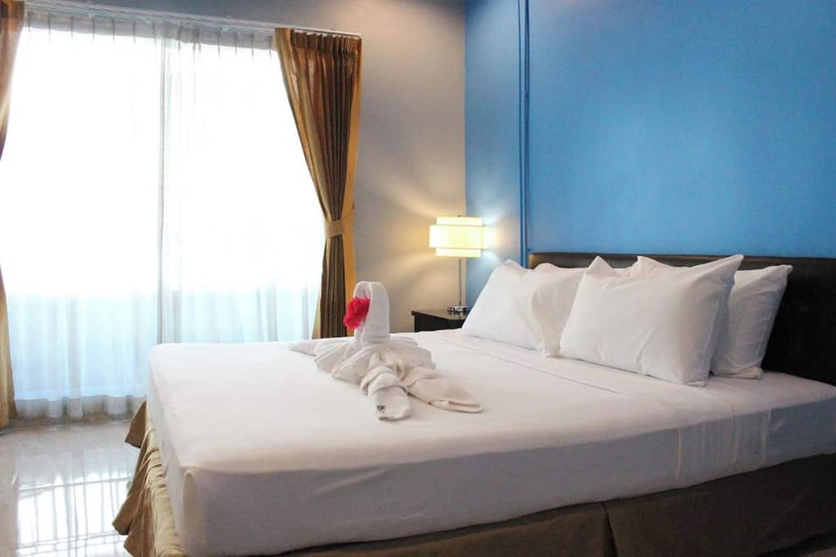 A hotel room with a neatly made bed, a lamp on the nightstand, and a window with curtains.