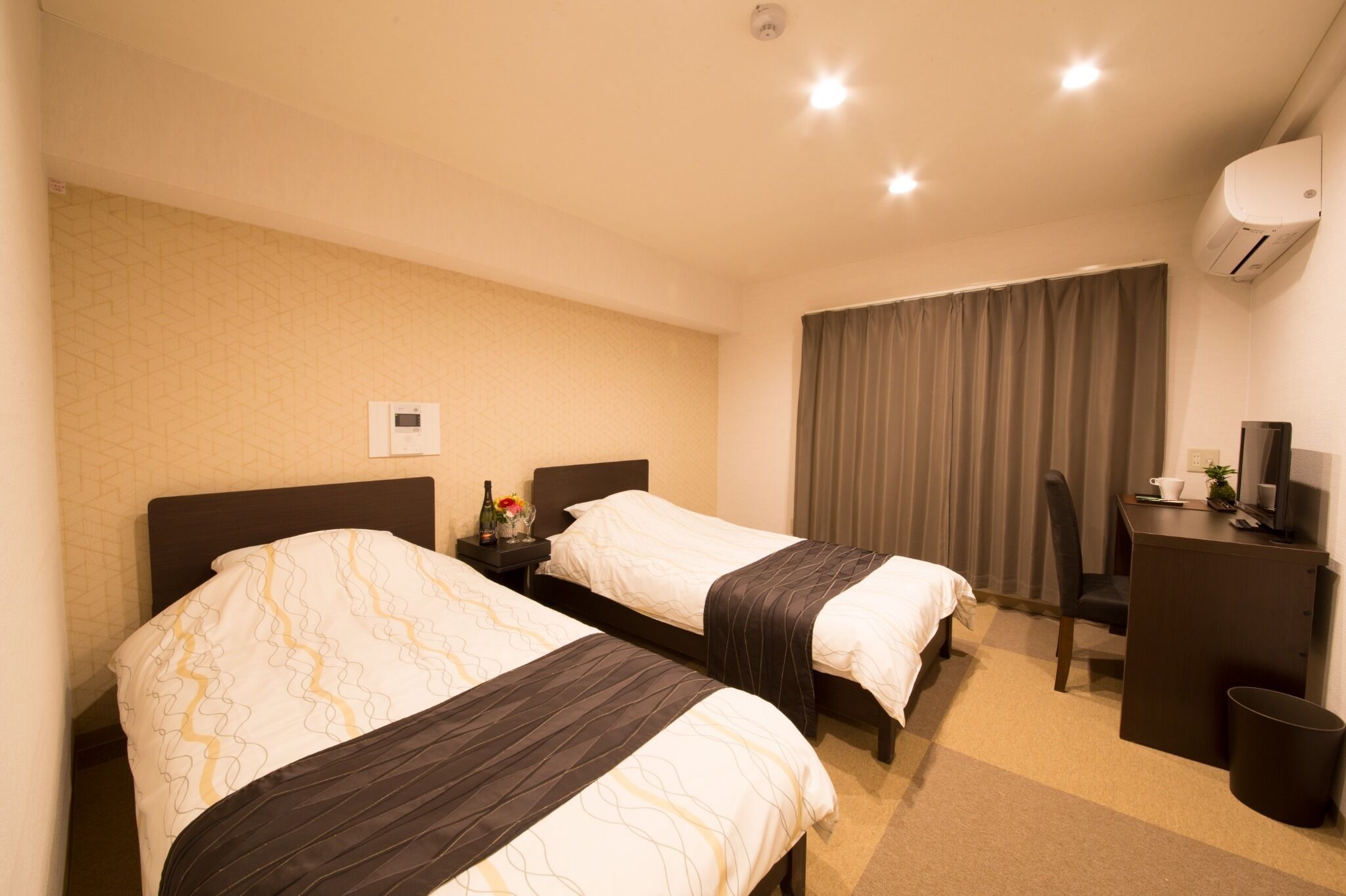 A hotel room with two beds, a desk, a chair, a trash bin, and an air conditioning unit.