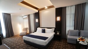 Une chambre d’hôtel avec un grand lit, un canapé, un bureau avec un panier de fruits et une chaise.