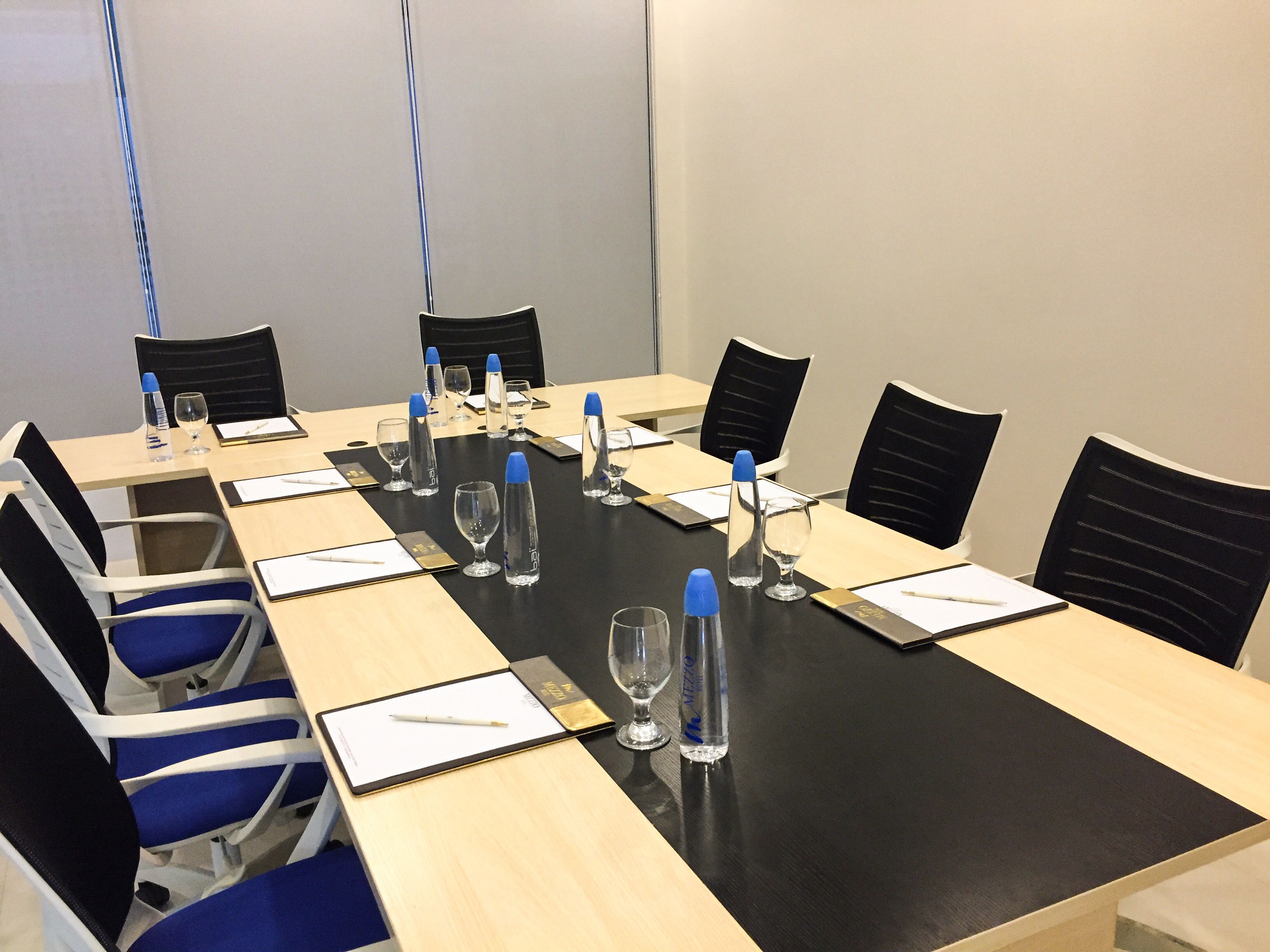 Ett konferensrum med ett långt bord, svarta stolar och vattenflaskor.