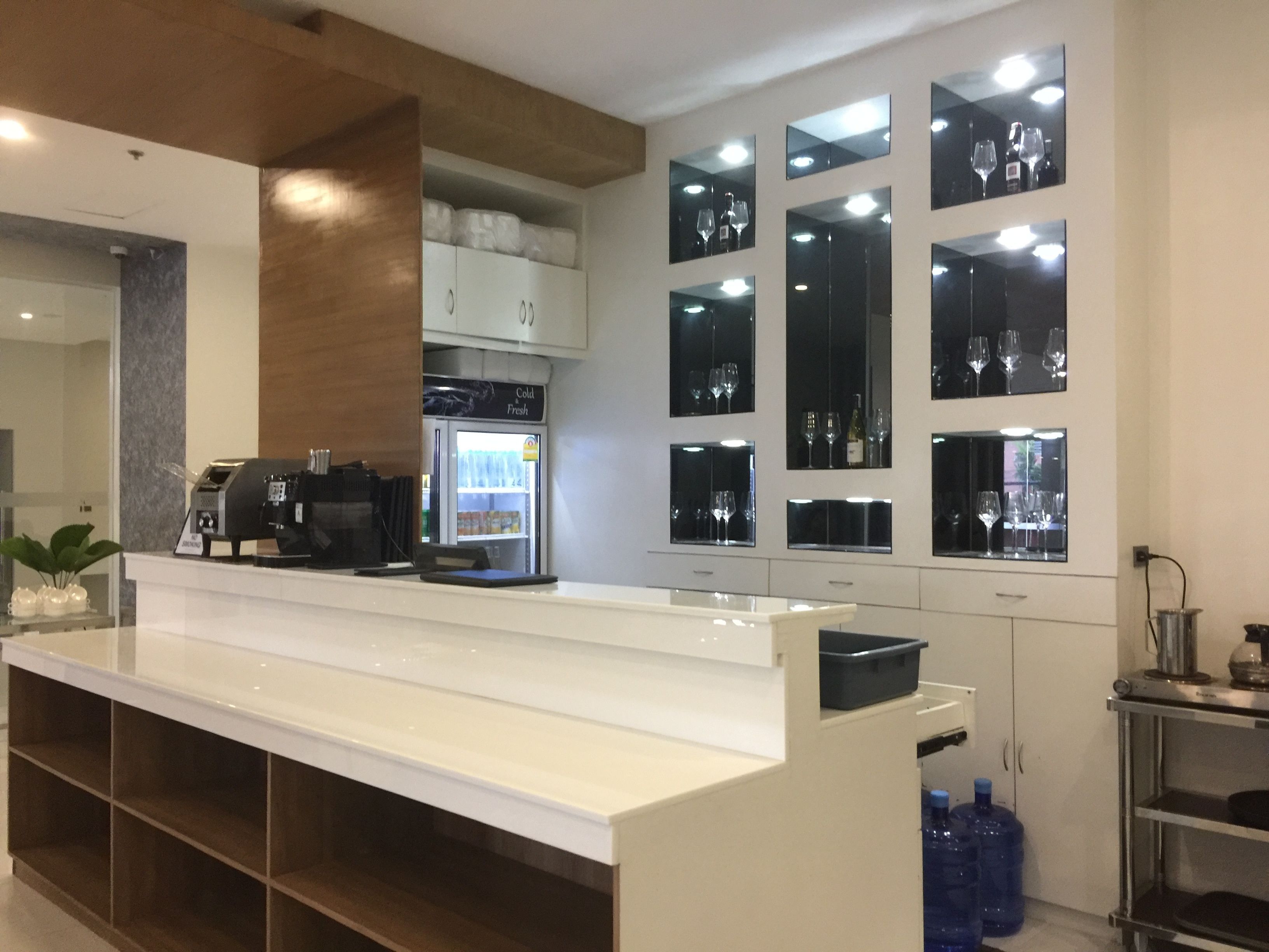 A modern kitchen with a white countertop, a coffee machine, a refrigerator, and a wine display.