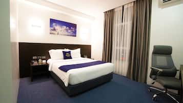 Hotelkamer met een groot bed, een bureau en een stoel. Er hangt een schilderij aan de muur en boven het bed bevindt zich een airconditioning.