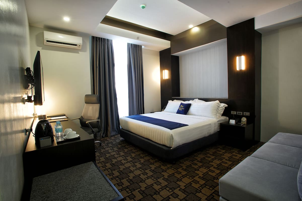 Quarto de hotel com cama, escrivaninha, cadeira, mesa de cabeceira e ar condicionado.